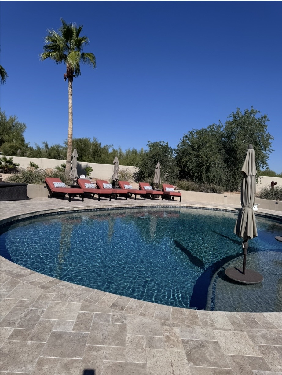 Finished Desert Chic pool deck with travertine tile and lounge chairs at golden hour