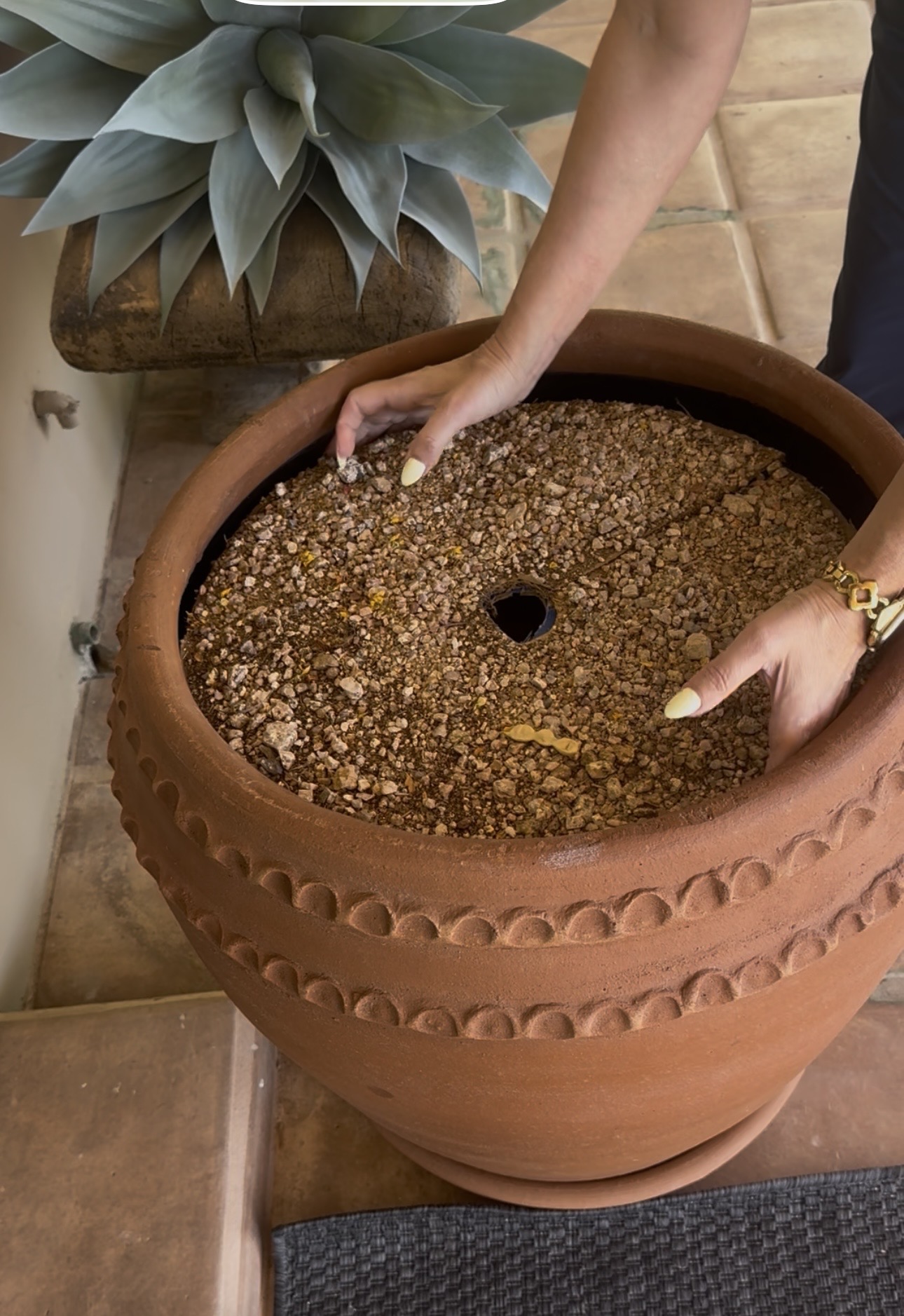 Hands placing the gravel-covered cardboard circle on top of the box inside the terracotta pot