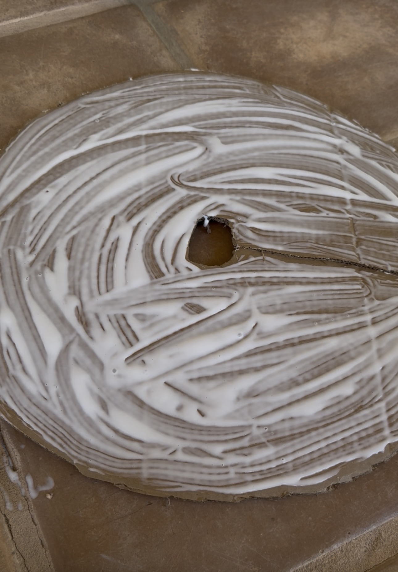 Cardboard circle insert covered in swirled white glue before gravel is added