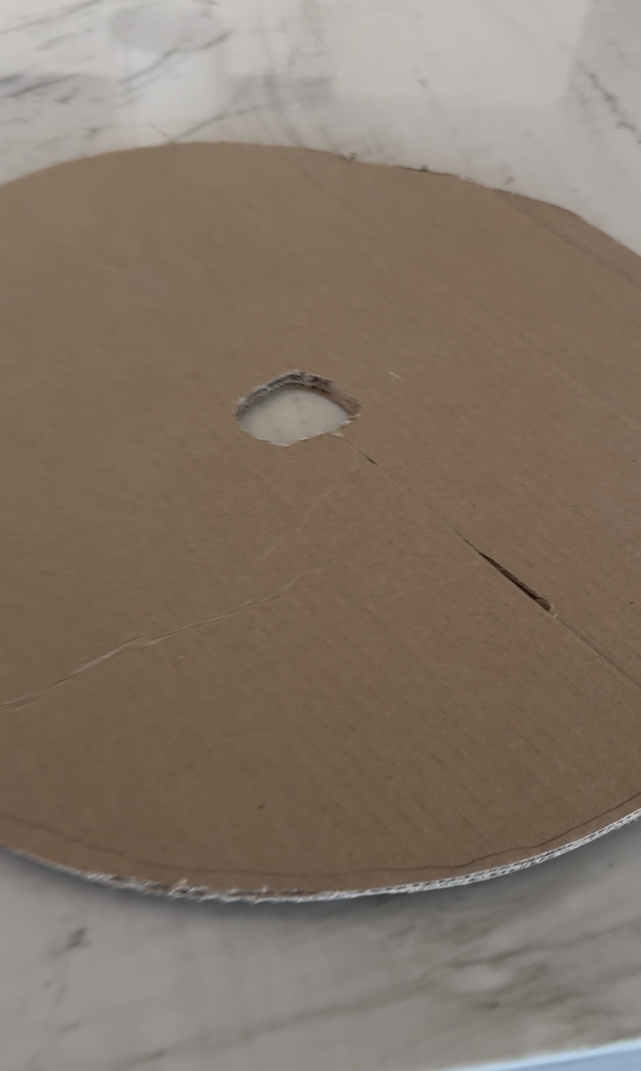 Round cardboard insert with a center hole and a straight cut line to the edge, resting on a marble countertop