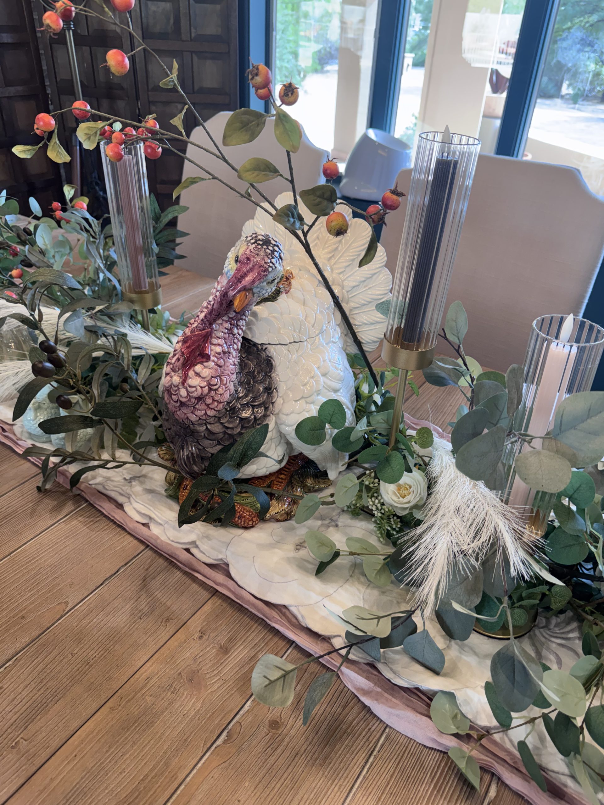 Ceramic heirloom turkey centerpiece surrounded by eucalyptus, berry branches, pampas and gold-trimmed glass candle holders